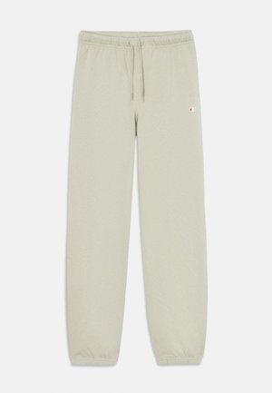 Lys beige joggebukser laget av myk materiale, med elastisk midjebånd og snøring, samt en brodert logo på lårets øvre del.
