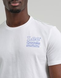 Uomo che indossa una t-shirt bianca con il logo blu "Lee Crayola" e un design a linee ondulate sulla parte superiore sinistra del petto, su uno sfondo grigio neutro.