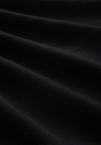Tissu noir avec une texture douce et lisse, présentant des motifs de vagues subtils créés par le drapage. Aucune quincaillerie ou accent visible.