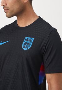 Black athletic shirt with textured fabric, blue Nike logo, and England crest. Features short sleeves and a crew neck design.