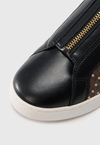 Baskets en cuir noir avec dessus texturé, semelle en caoutchouc blanche, détail de fermeture éclair dorée et petits clous métalliques sur le côté pour un accent supplémentaire.