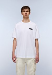 Hvid bomulds t-shirt med rund hals og korte ærmer. Har et sort rektangulært logo på venstre bryst. Glat tekstur.