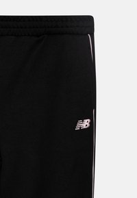 Crne sportske hlače s mekanom teksturom, s ružičastim izvezenim logotipom i bijelim bočnim trakama. Elastični pojas za udobnost.