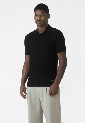Tricou polo negru cu mâneci scurte și model tricotat texturat, având un guler clasic și un design mulat. Asortat cu pantaloni deschiși la culoare.