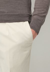 Grauer gestrickter Pullover mit Rippbündchen und Saum, kombiniert mit cremefarbenen Hosen mit seitlichen Taschen. Glatte und lässige Stoffstruktur.