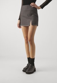 Mini falda gris con una abertura lateral, adornada con tachuelas plateadas a lo largo del dobladillo. Combinada con calcetas negras y zapatos negros de suela gruesa.