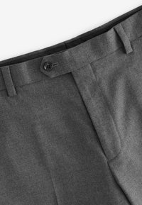 Gros plan sur la ceinture et la fermeture à bouton sur un pantalon gris foncé sur mesure avec passants de ceinture et braguette zippée dissimulée.