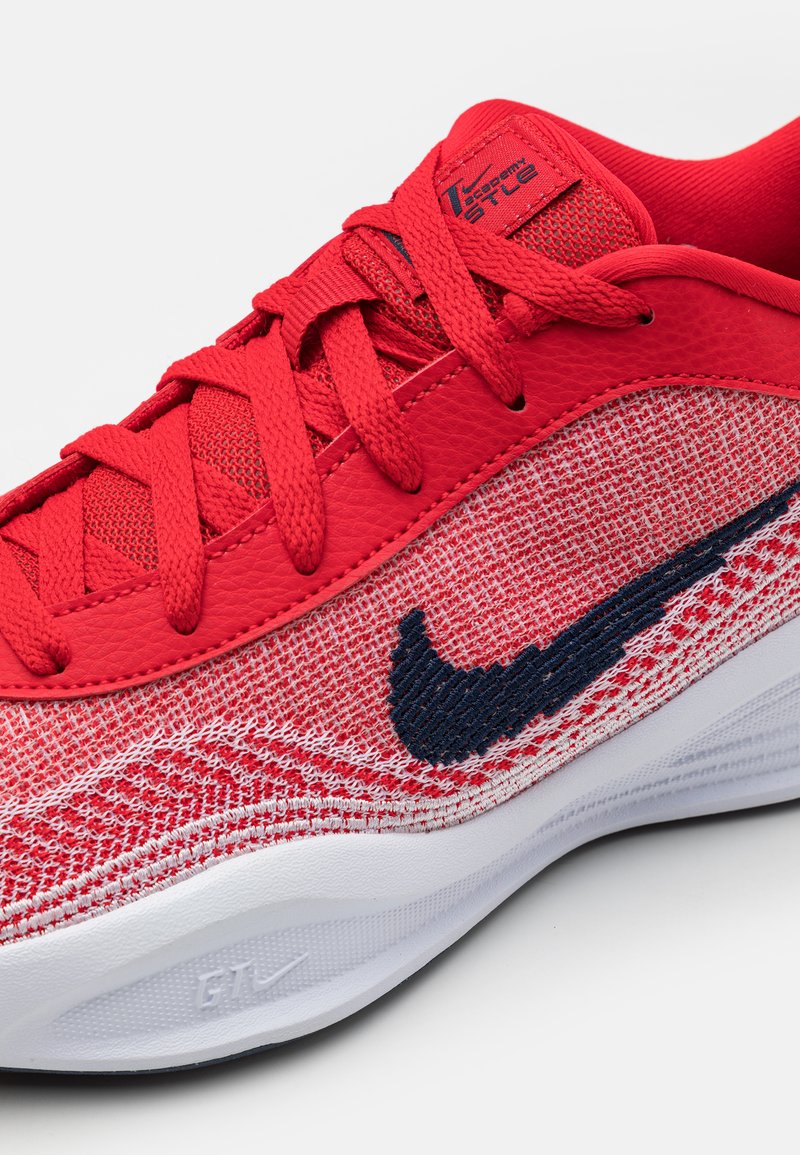 Czerwony but sportowy z teksturowanym siateczkowym wierzchem i gładkimi syntetycznymi akcentami, z czerwonymi sznurowadłami i granatowym logo typu swoosh. Biała podeszwa.