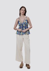 Blusa floral con tirantes ajustables, diseño peplum, en tonos azules y amarillos, combinada con pantalones de pierna ancha color crema y sandalias de plataforma marrones.
