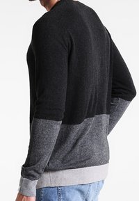 Mäns tröja i mörkgrå och ljusgrå, med en färgblockdesign, långa ärmar och ribbad manschett och nederkant. Mjuk stickad textur.