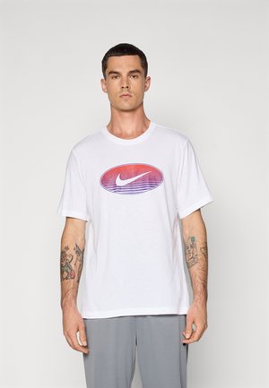 Hvid bomulds t-shirt med et stort, gradient Nike-logo i rød og violet. Korte ærmer og en afslappet pasform. Grå bukser bæres under.