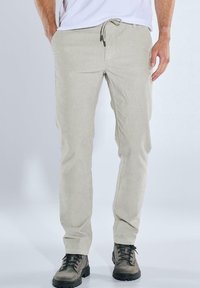 Beige Cordhosen mit einem Kordelzugbund, schmalem Schnitt, seitlichen Taschen und dezent strukturiertem Stoff, kombiniert mit schwarzen Schnürboots.