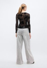 Μαύρο διαφανές τοπ με λουλουδάτο μοτίβο και μακριά μανίκια, συνδυασμένο με ανοιχτό γκρι παντελόνι φαρδιάς γραμμής με πίσω τσέπες και άνετη εφαρμογή.