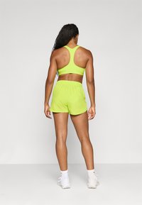 Neon zelena sportska grudnjak i odgovarajuće kratke hlače napravljene od laganog materijala, s dizajnom racerback i elastičnom trakicom u struku, upotpunjene bijelim tenisicama.