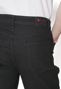 Pantalones de mezclilla negros con una textura suave, que presentan una etiqueta en la cinturilla con el nombre "DENIM PROJECT" y un diseño clásico de cinco bolsillos.