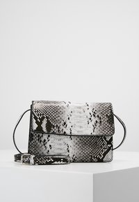 Černobílá taška přes rameno s vzorem hadí kůže, obdélníkového tvaru, s klopou a nastavitelným popruhem na bílém povrchu.