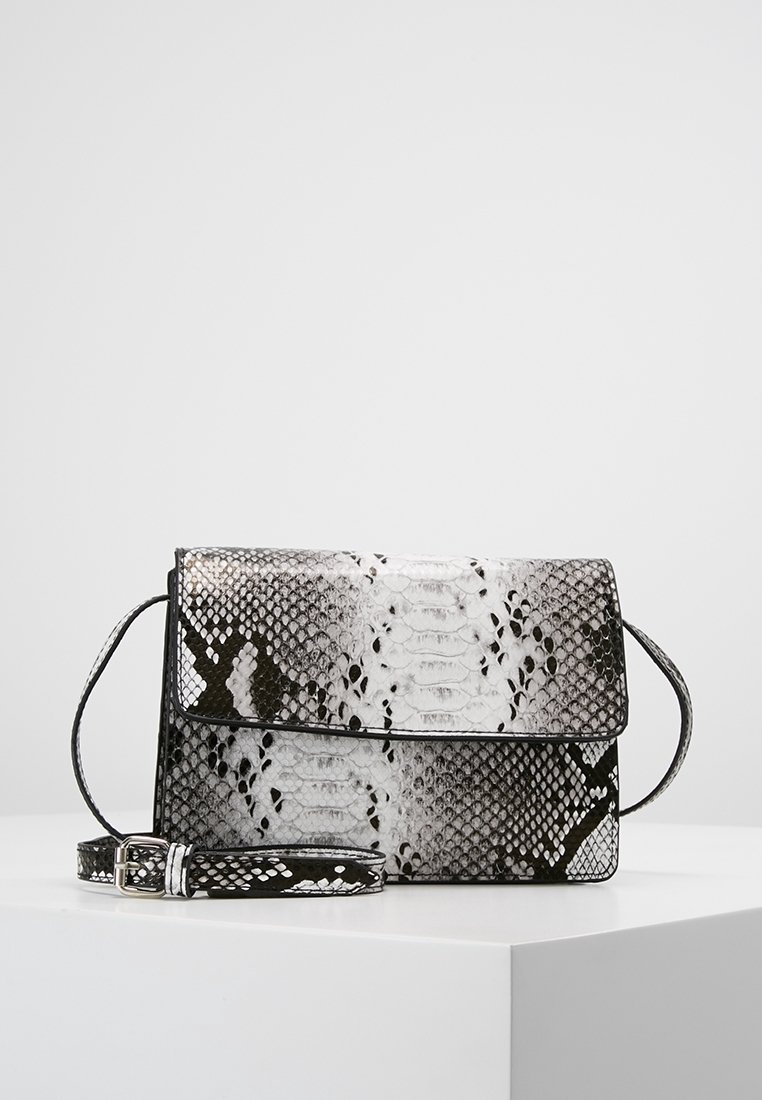 Černobílá taška přes rameno s vzorem hadí kůže, obdélníkového tvaru, s klopou a nastavitelným popruhem na bílém povrchu.