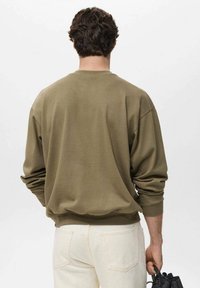 Olijfgroen sweatshirt met ronde hals, lange mouwen, zachte textuur, ontspannen pasvorm en geribde manchetten, gedragen met lichte jeans.