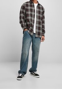 Camisa de franela a cuadros en negro, blanco y rojo, combinada con unos vaqueros de denim azul claro y zapatillas negras con detalles en blanco. Ajuste casual.