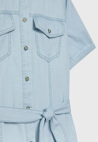 Vaaleansininen farkku mekko, jossa on lyhyet hihat, kaksi rintataskua, edessä napit ja vyö vyötäröllä. Pehmeä rakenne ja rento muotoilu.