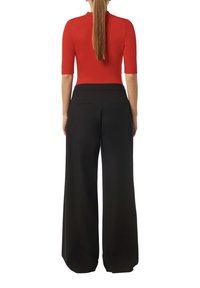 Top rojo ajustado con mangas cortas combinado con pantalones negros de pierna ancha y cintura alta. Textura suave, detalles mínimos y forma entallada.