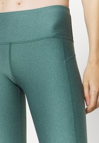 Zielone legginsy z wysokim stanem, wykonane z elastycznej, fakturowanej tkaniny, z płaskimi szwami i boczną kieszenią dla wygody.