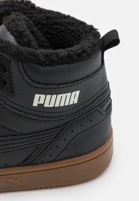 Czarne skórzane sneakersy z futrzanym czarnym wykończeniem, gumową podeszwą i wyraźnym białym logo "PUMA" z boku.
