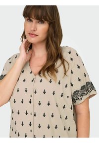 Beige blúz fekete geometrikus hímzéssel az ujjakon és az elején. Röpke ujjak, V-nyakkivágás és gombos zárás. Puha, könnyű anyag.