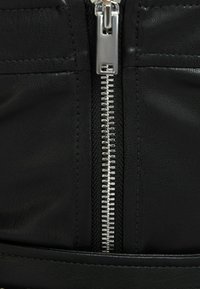 Material de cuero sintético negro con una cremallera plateada que corre verticalmente. Presenta detalles cosidos y una textura suave.