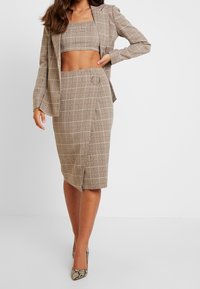 Braun karierter zweiteiliger Anzug mit einem cropped Top und einem knielangen Rock mit runder Akzentuierung. Die Textur wirkt glatt und maßgeschneidert.