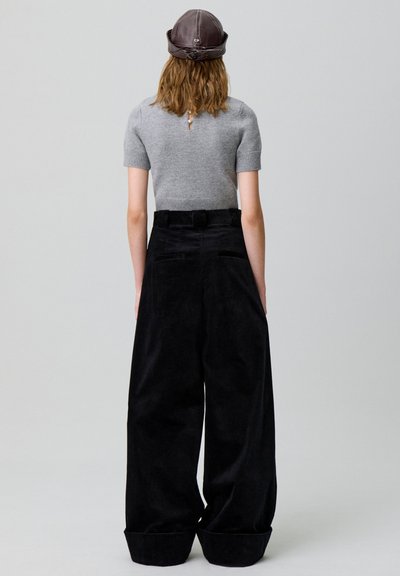 Top de punto gris de manga corta combinado con pantalones de pana negros de pierna ancha. Los pantalones cuentan con bolsillos traseros y una cintura alta.