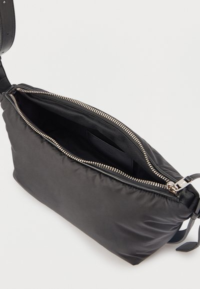Μαύρο ορθογώνιο τσαντάκι ώμου με ανοιχτό ασημένιο φερμουάρ, που δείχνει το άδειο εσωτερικό και μια μικρή εσωτερική τσέπη.