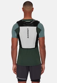 Black and white Mammut vest with adjustable straps, streamlined design, and a hydration tube, worn over a green shirt.