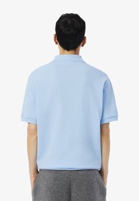 Ljusblå pikétröja med standardkrage, korta ärmar och en mjuk textur. Har nederkant med rak form och en avslappnad passform.