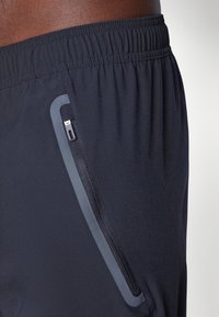 Marineblaue Sportshorts mit elastischem Bund. Verfügt über eine Reißverschlusstasche und einen glatten, leichten Stoff mit einem dezenten Glanz.
