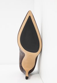 Chaussure à talon haut à bout pointu avec dessus marron texturé et semelle beige comportant un large patin antidérapant noir sur la face inférieure.