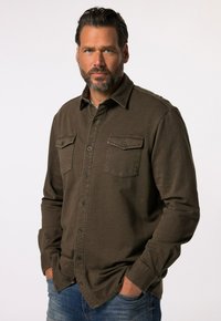 Olijfgroene button-up shirt met twee borstzakken, duurzame stof, lange mouwen en een kraag. Draagt het met blauwe jeans.