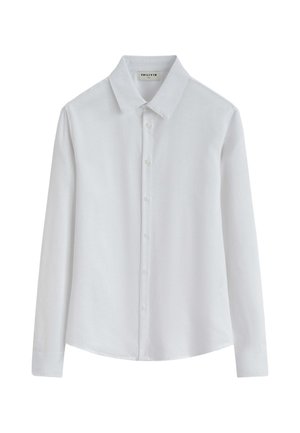 Chemise blanche à manches longues avec col, boutons sur le devant et ourlet droit, présentée sur un fond uni.