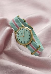 Timex Marlin-horloge met goudkleurige kast, muntgroene wijzerplaat, zwarte cijfers en stoffen band met groene, witte en roze strepen op een roze stoffen achtergrond.