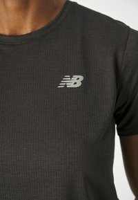 T-shirt de sport noir avec un motif texturé, encolure ronde et logo argenté New Balance sur le côté supérieur gauche.