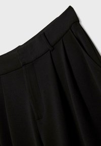 Pantalon noir taille haute avec plis, passants de ceinture et détail de poche latérale sur un fond uni clair.