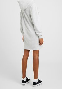 Vestido sudadera gris con mangas largas, corte relajado y bolsillos laterales. Combinado con zapatillas negras y calcetines tobillero blancos. Textura de tela suave.