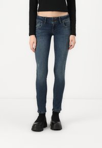Skinny fit jeans in dark blue denim. Features a classic five-pocket design and slight distressing. Paired with black platform shoes.
