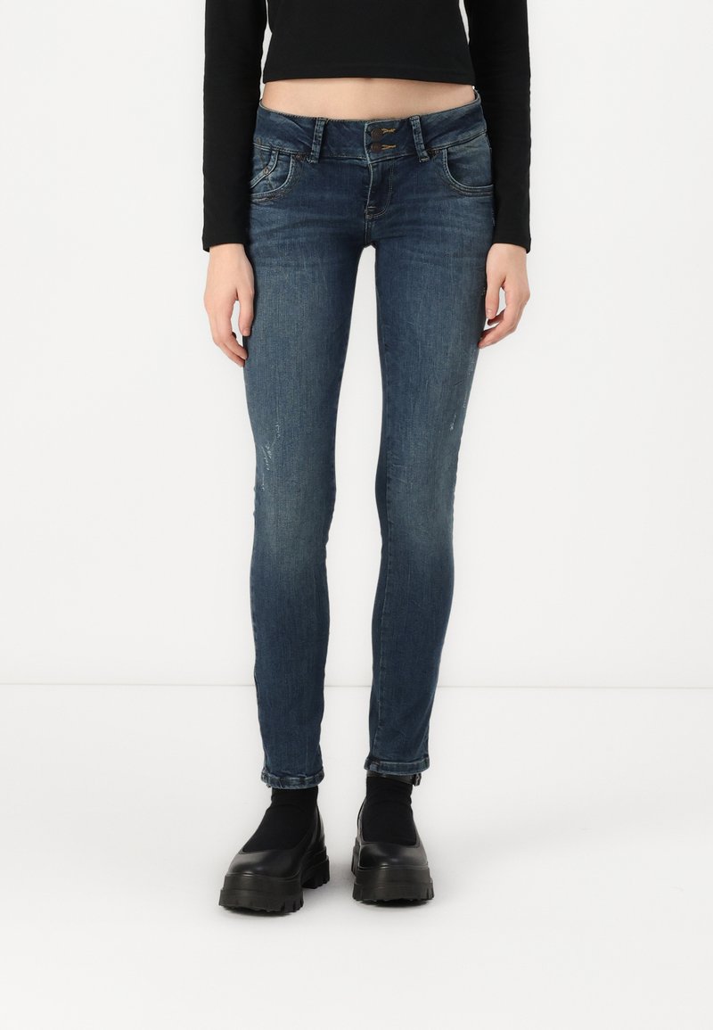 Skinny fit jeans in dark blue denim. Features a classic five-pocket design and slight distressing. Paired with black platform shoes.