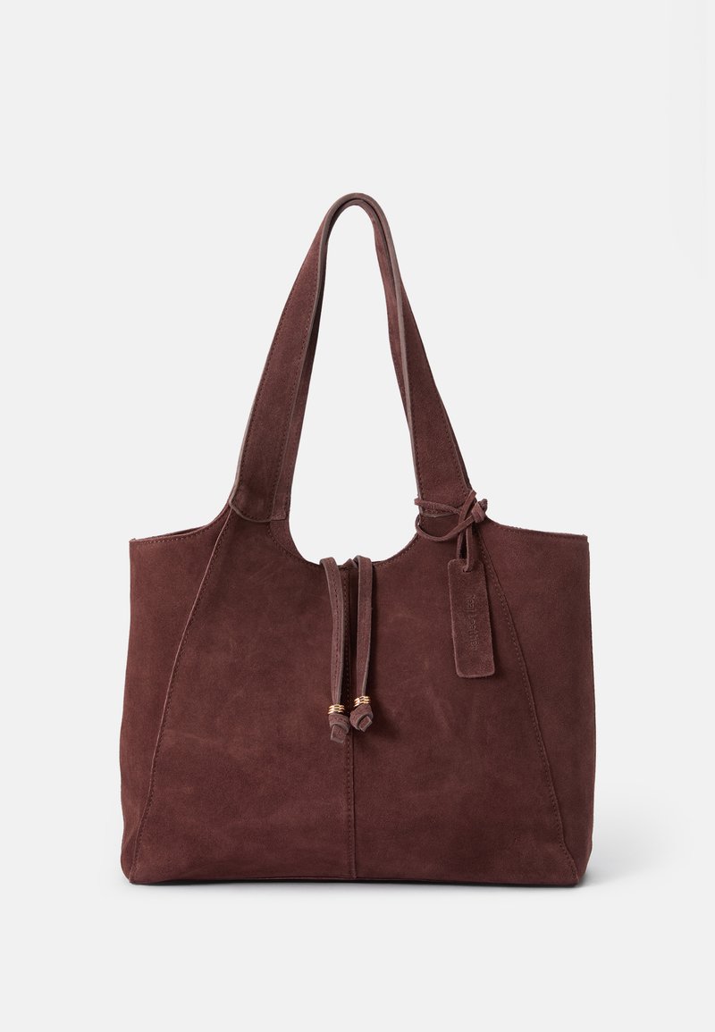 Αυτή η σουέντ τσάντα tote σε σκούρο μπορντό διαθέτει δύο μακριές λαβές, κλείσιμο με κορδόνι και μια μικρή ετικέτα που προσαρτάται, με λεία υφή.