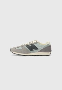 Baskets de sport grises et turquoise avec une tige en daim et textile, dotées d'un logo noir, de lacets blancs et d'une semelle extérieure texturée.
