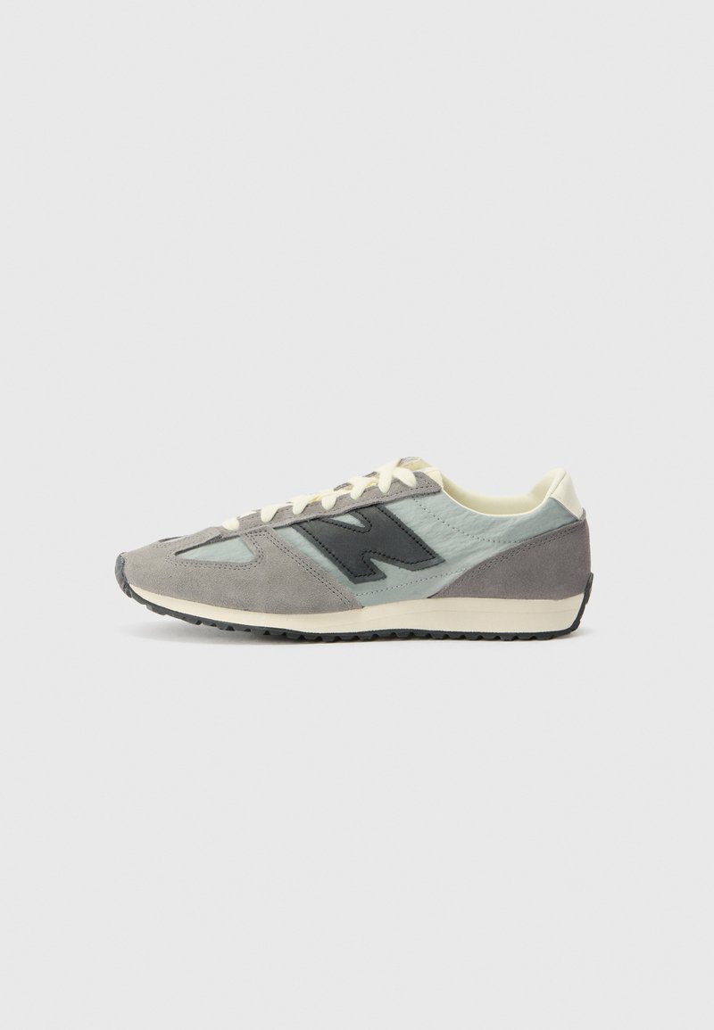 Baskets de sport grises et turquoise avec une tige en daim et textile, dotées d'un logo noir, de lacets blancs et d'une semelle extérieure texturée.