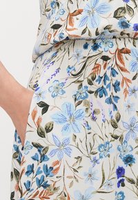 Ύφασμα με ανθικό μοτίβο και ανοιχτό μπεζ φόντο, που περιλαμβάνει μπλε, πράσινα και καφέ λουλούδια. Διαθέτει πλαϊνή τσέπη. Απαλό, ελαφρύ υλικό.