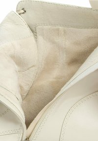 Interior de bolso de cuero beige con forro de piel suave, con cierre de cremallera y textura lisa. Incluye un bolsillo para organización.