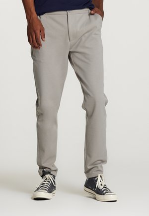 Pantalones de chándal gris claro con un ajuste tapered, textura suave y frontal plano. Combinados con zapatillas negras de caña alta con suelas y cordones blancos.